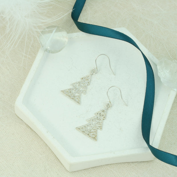 Silver hook earrings in the shape of a Christmas three with three layers. The trees feature a hand drawn pattern which is hand sawn with swirls from the centre to the sides. They have a hammered texture which has been polished to a shiny finish, giving them a shimmer effect. 