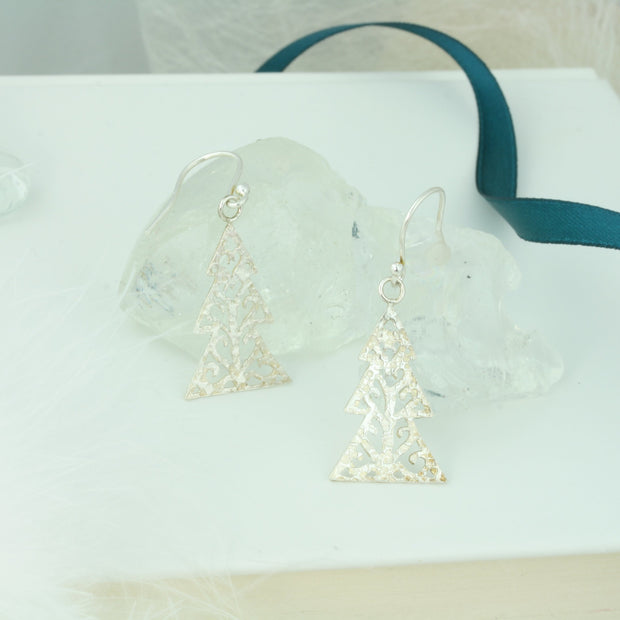 Silver hook earrings in the shape of a Christmas three with three layers. The trees feature a hand drawn pattern which is hand sawn with swirls from the centre to the sides. They have a hammered texture which has been polished to a shiny finish, giving them a shimmer effect. 