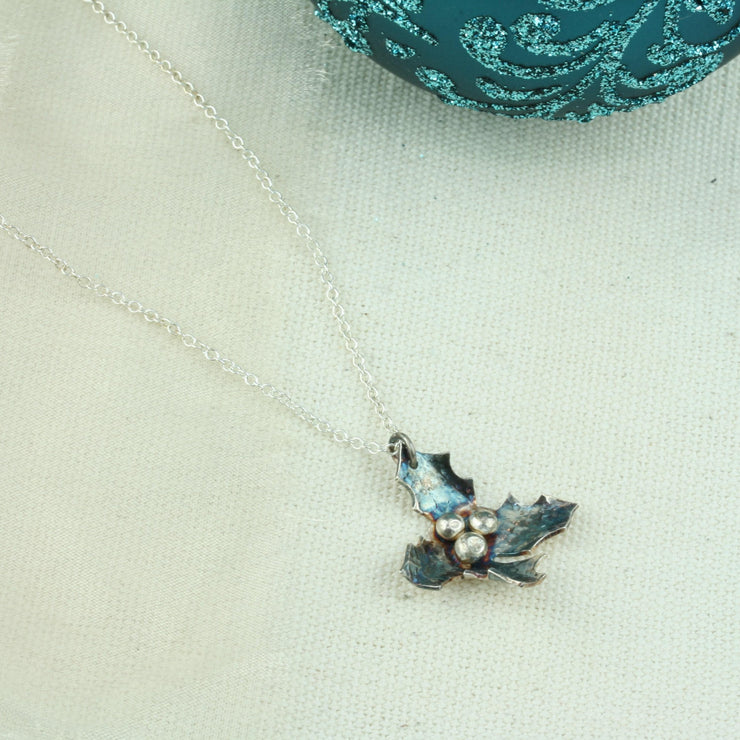 Silver holly pendant necklace. Featuring holly with four leaves with a hammered texture and aged darker finish, polished to a shine. And three shiny silver berries in the centre.