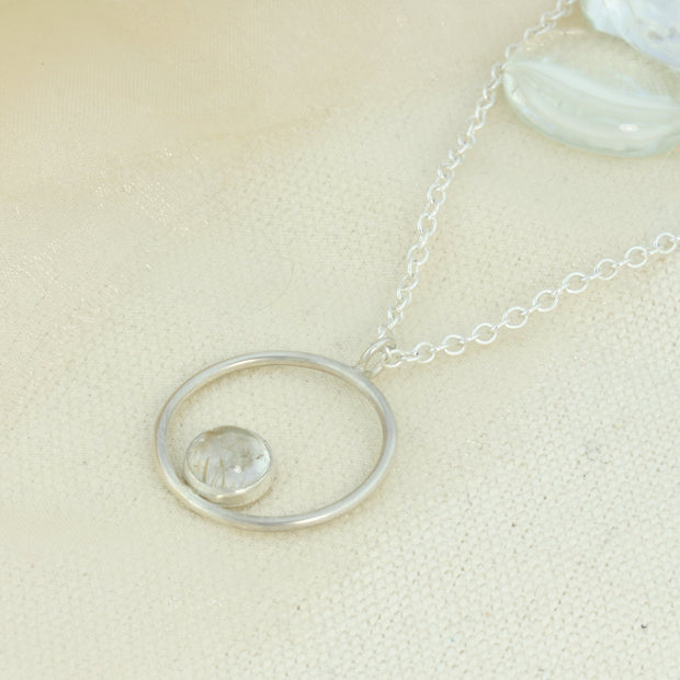 Silver pendant necklace featuring a hoop with a gemstone in inside at the bottom. The gemstone measures 8mm in diameter. This pendant features a Golden Rutile Quartz cabochon gemstone, other options are available.