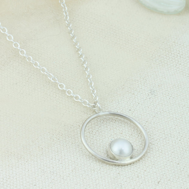 Silver pendant necklace featuring a hoop with a gemstone in inside at the bottom. The gemstone measures 8mm in diameter. This pendant features a freshwater pearl, other options are available.