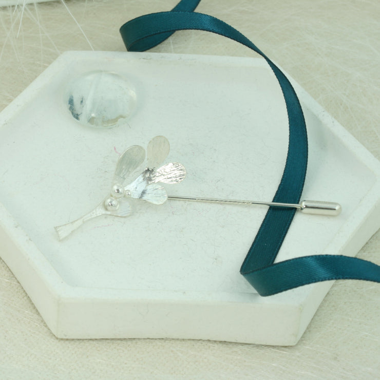 Silver pin featuring a Mistletoe shape with five small leaves and three berries at the top. It is 3.5 x 2 cm in size and the 5cm long pin at the back comes with a pin protector to pop onto the sharp end. All polished to a mirror finish, with a striped hammered texture on the front of the leaves. Lovely on a hat, scarf, or jacket.