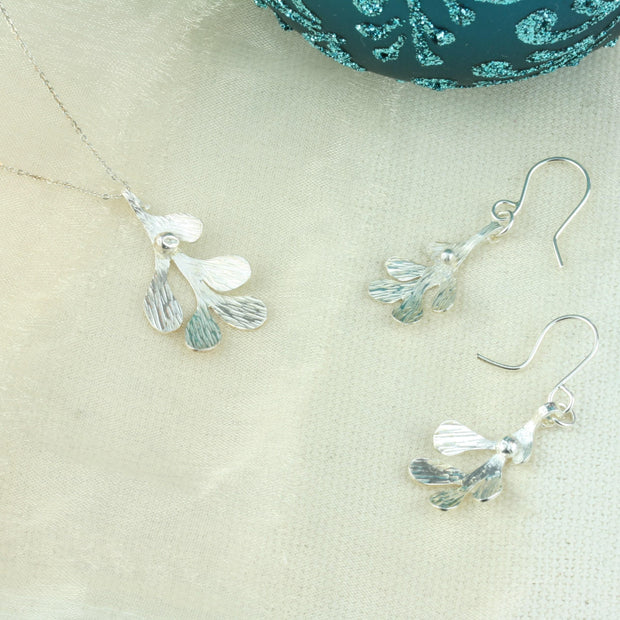 Silver hook earrings featuring Mistletoe with a silver ball as a berry. The leaves have a striped texture and a shiny silver finish. The total drop is 2.5cm from the hook. Seen here with the matching pendant necklace.