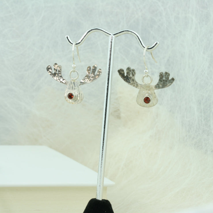 Silver hook earrings featuring a sawn out Rudolph head. The face has a striped texture and shiny silver finish. The Antlers have a round hammered texture and are aged to give them a darker look, they have been polished to a shine. The red nose is a Garnet gemstone set in a tube setting. A matching pendant necklace and ring are available as well. 