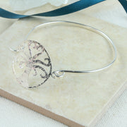 Silver bangle bracelet featuring a TRee of Life at the front. The wire of the bangle is fastened on one side of the Tree of Life. The other side can be looped through the jump ring attached to the Tree of Life to open and close the bangle bracelet. It is made from eco silver and has a shiny finish. The Tree of Life has a hammered texture.