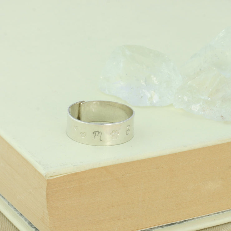 Personalised silver wrap ring. The ring is made from eco silver and 7mm wide. This ring is personalised with some hearts and a paw, with the letters M and B on either side. The ring is left oen and is adjustable, making it comfortable whether it&