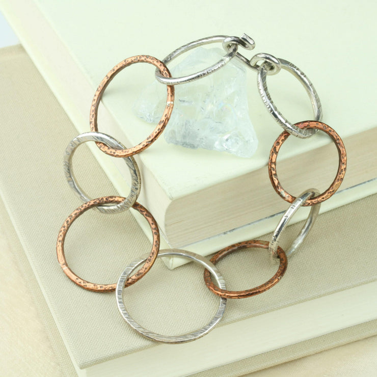 Silver and copper bracelet featuring nine hoops in various sizes. All hoops have a hammered texture and shiny finish. A matching statement necklace is available as well.