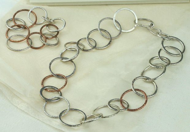 Silver and copper bracelet featuring nine hoops in various sizes. All hoops have a hammered texture and shiny finish. A matching statement necklace is available as well. Seen here with the matching necklace.