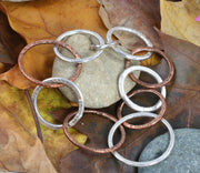 Silver and copper bracelet featuring nine hoops in various sizes. All hoops have a hammered texture and shiny finish. A matching statement necklace is available as well.