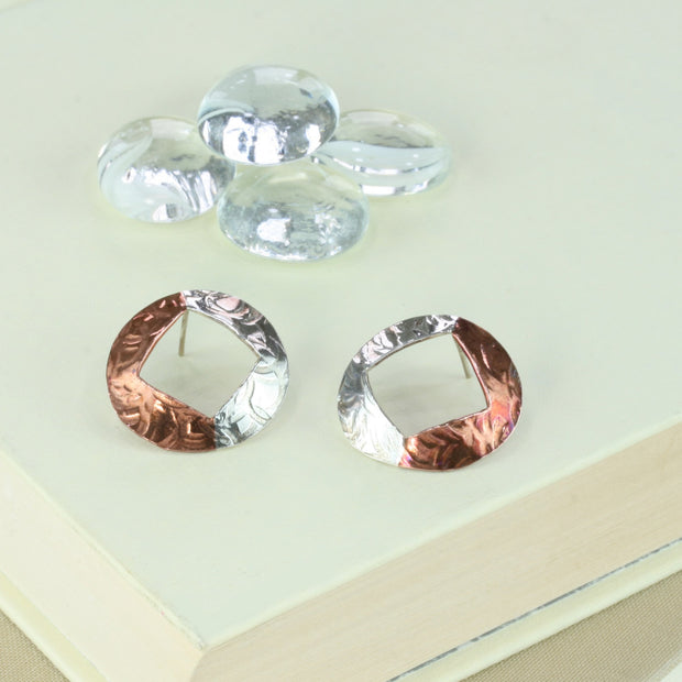 Large stud earrings with copper and silver. A large circle shape with a square diamond shape sawn out of the centre. One side is made in copper the other in silver. Available with two textures, a striped texture and a round circle texture.