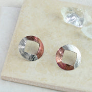 Large stud earrings with copper and silver. A large circle shape with a square diamond shape sawn out of the centre. One side is made in copper the other in silver. Available with two textures, a striped texture and a round circle texture.