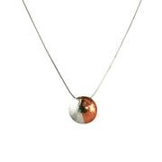 Silver and copper pendant necklace. A round domed pendant with one half in copper and the other in silver. This necklace has a wide subtle striped finish, a sharper striped finish version is available as well. It comes with a snake chain necklace.