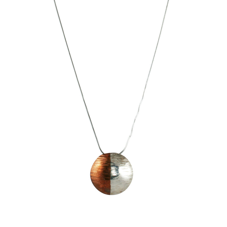 Silver and copper pendant necklace. A round domed pendant with one half in copper and the other in silver. This necklace has a sharp striped finish, a wider subtle striped finish version is available as well. It comes with a snake chain necklace.