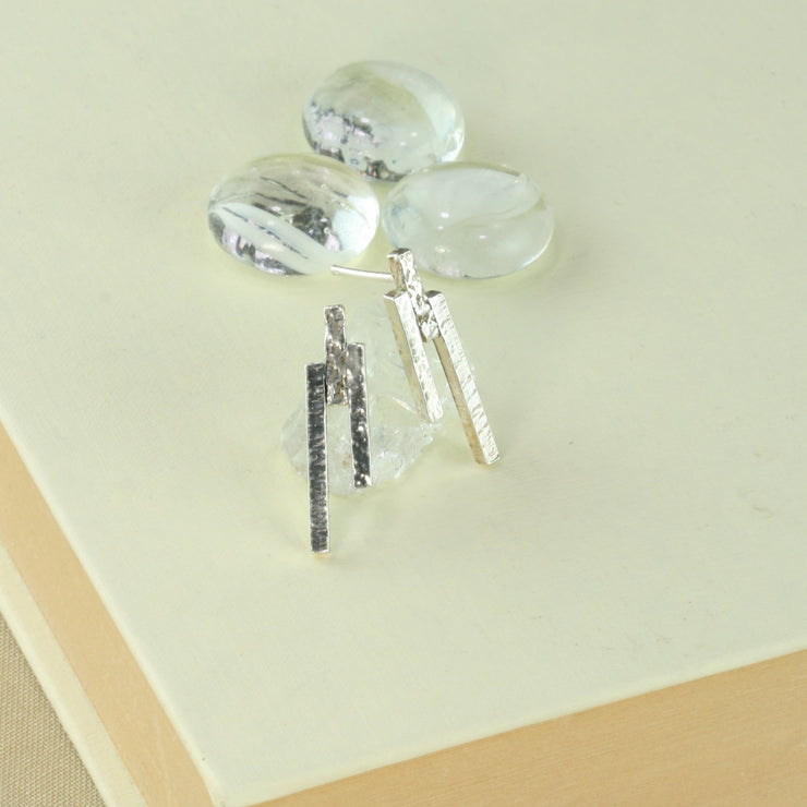 Eco silver stud earrings featuring three bars with different lenghts and textures. They have been placed at different heights.