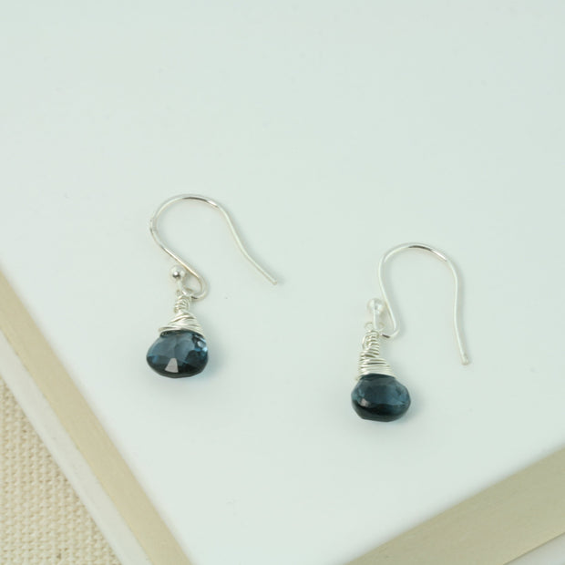Silver briolette earrings featuring London Blue Topaz faceted heart gemstones. The facets point at different angles catching the light perfectly for a bit shimmer and shine. They are wrapped with eco silver wire and dangle from silver earrings hooks.