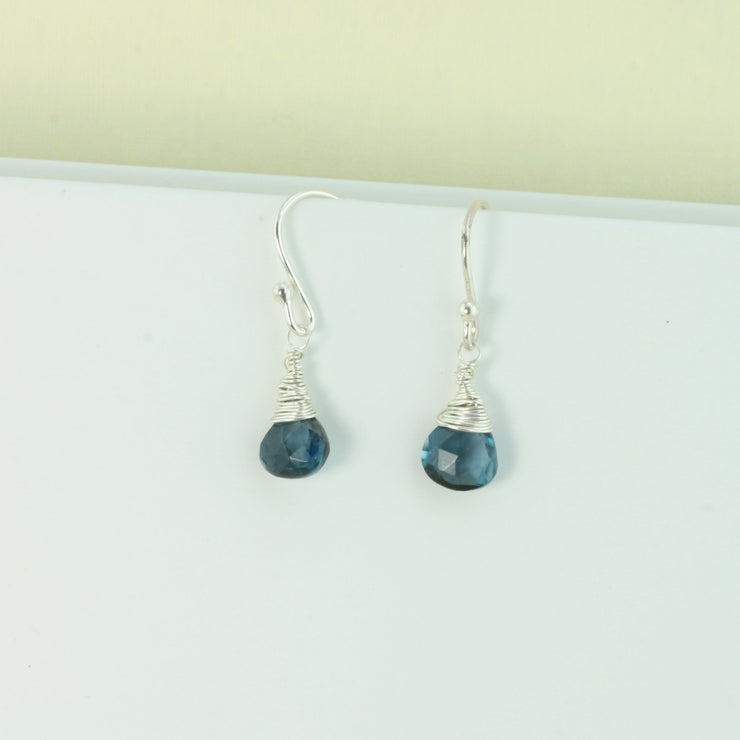 Silver briolette earrings featuring London Blue Topaz faceted heart gemstones. The facets point at different angles catching the light perfectly for a bit shimmer and shine. They are wrapped with eco silver wire and dangle from silver earrings hooks.