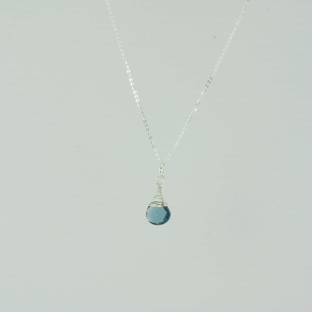 Silver briolette pendant necklace featuring a London Blue Topaz faceted heart gemstone. The facets point at different angles catching the light perfectly for a bit shimmer and shine. It is wrapped with eco silver wire and dangles from a delicate silver necklace.