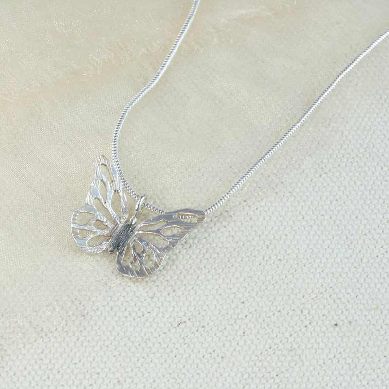 Silver hand sawn butterfly. It has a striped texture and a shiny silver finish. Apart from the body which has been oxidised slightly to give it a darker look. The nexklace is made of snake chain and closes with a lobster clasp.