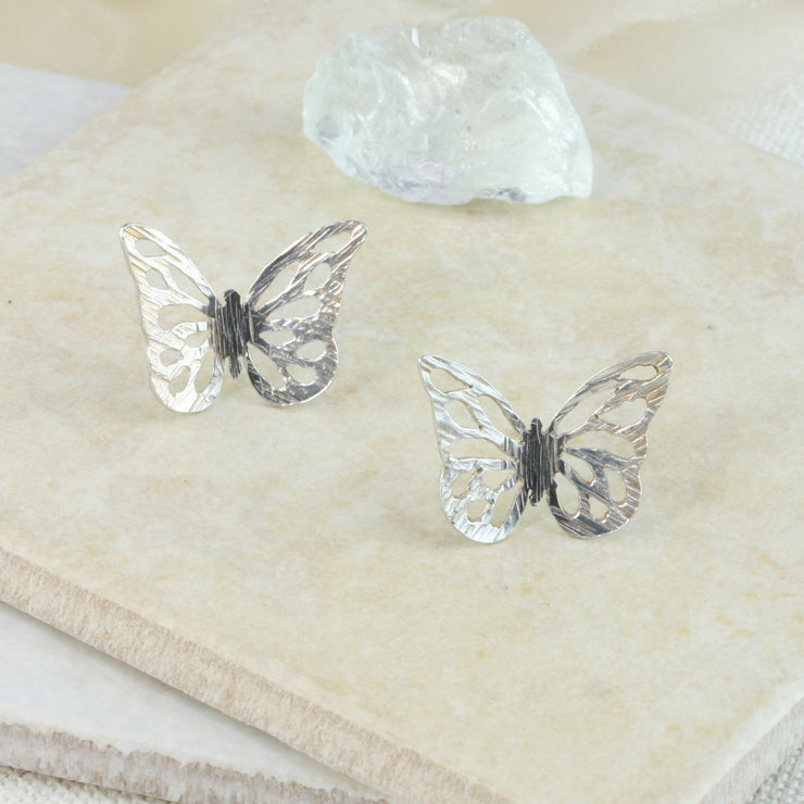 Eco silver butterfly stud earrings. The pattern is sawn out by hand and the striped texture and shiny finish give these butterflies a shimmering finish. The body has a darker oxidised finish.