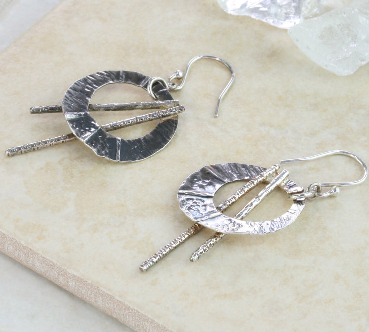 Silver hook earrings featuring open circles that have three folds from top to bottom and a round hammered texture. They have a darker oxidised finish. The two bars have a hammered texture and shiny silver finish.