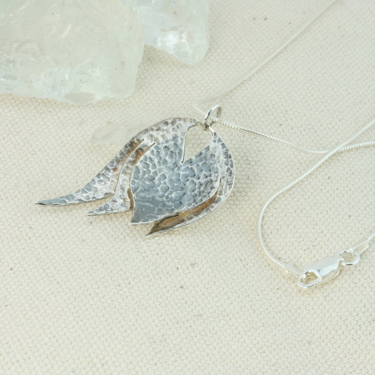 Silver pendant necklace featuring a petal pendant that has been slightly domed and textured. The heart of the petal has a darker oxidised finish. The pendant has a shiny finish and is featured by a snake chain with a lobster clasp fastening.