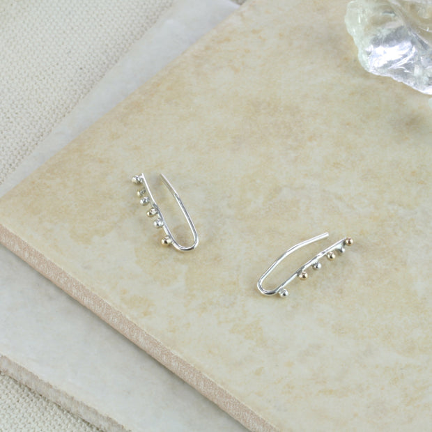 Silver ear climbers made from silver wire that hooks through the ear. Three silver and three 9ct gold balls are attached to the front of the earrings. They have a shiny mirror finish. They hug the ear and are adjustable by pinching them slightly.