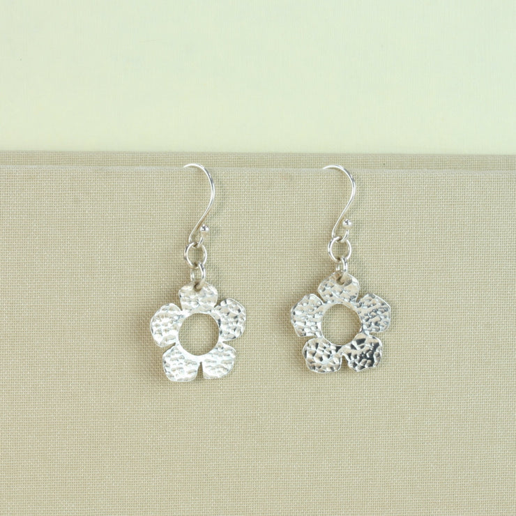 Silver hook earrings featuring a flower shape with 5 petals each and a hammered shiny finish at the front and a mirror finish at the back.