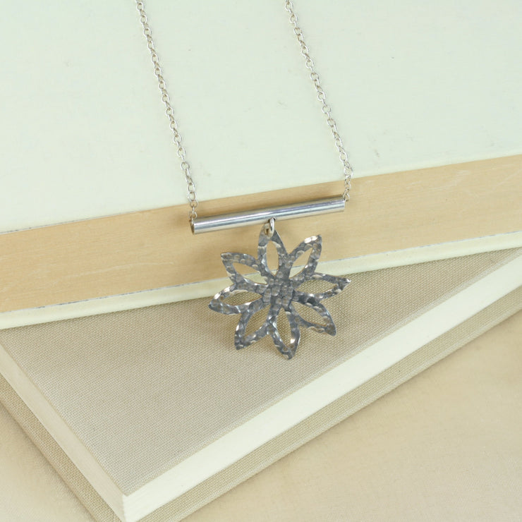 Silver pendant necklace with a flower shape with pointed sharp petals dangling off a round branch. The pendant and necklace have a shiny finish.