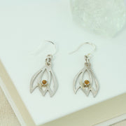 Silver flower bud silhouette hook earrings featuring three sawn out leaves with a Citrine gemstone in a tube setting at the bottom in the middle leaf. The silver has a shiny mirror finish.