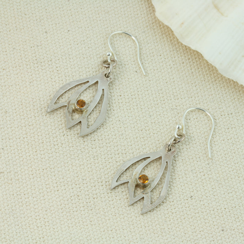 Silver flower bud silhouette hook earrings featuring three sawn out leaves with a Citrine gemstone in a tube setting at the bottom in the middle leaf. The silver has a shiny mirror finish.