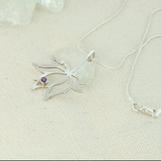 A silver pendant necklace featuring the silhouette of a flower with 3 petals and two leaves on both sides. The middle petal holds an Amethyst gemstone in a tube setting in place, at the tip inside the flower. The necklace is a snake chain with a lobster clasp.