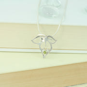 Silver pendant featuring a flower silhouette with a flower bud in the middle and a leaf on either side. The bottom of the flower bud features a peridot gemstone set in a tube setting. It has a mirror finish. The necklace is a snake chain with a lobster clasp fastening.