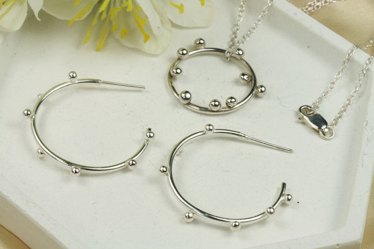 Set of large silver hoop earrings with 7 silver balls on each hoop. And a silver hoop pendant necklace featuring 9 silver balls. They&