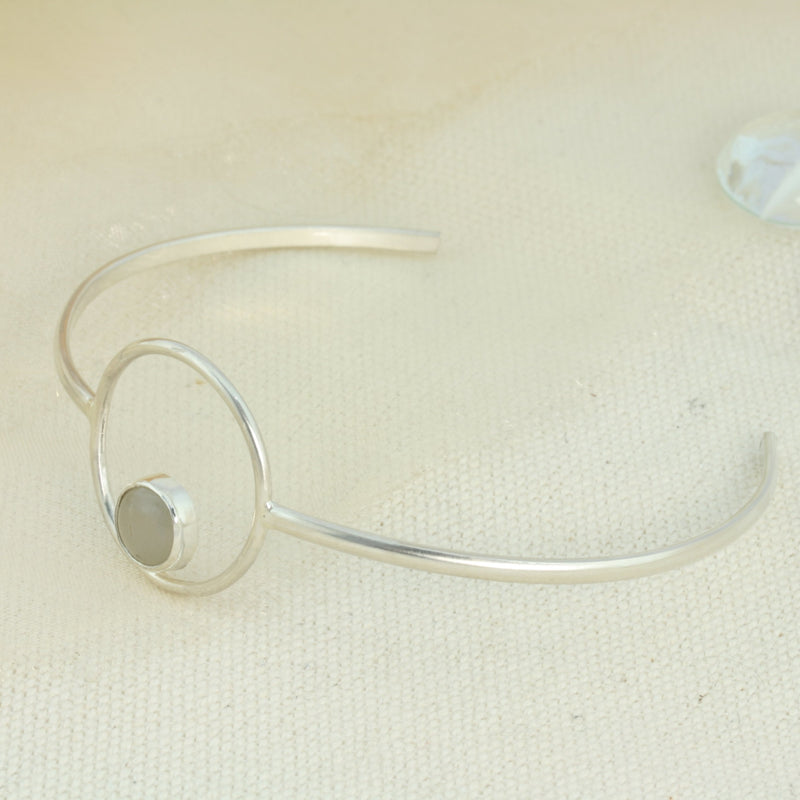 Silver bangle bracelet featuring a hoop in the centre. The hoop features a gemstone in the bottom centre, the gemstone is 8mm in diameter. This bangle features a Grey Moonstone. The silver is polished to a shiny matte finish.