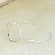 Silvere bangle bracelet featuring a hoop of 2cm in diameter in the middle of the bangle. The hoop features 6 silver balls hand placed around the bottom left of the hoop. In the middle of the balls sits a 3mm Garnet gemstone. 