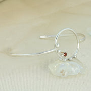 Silvere bangle bracelet featuring a hoop of 2cm in diameter in the middle of the bangle. The hoop features 6 silver balls hand placed around the bottom left of the hoop. In the middle of the balls sits a 3mm Garnet gemstone. 