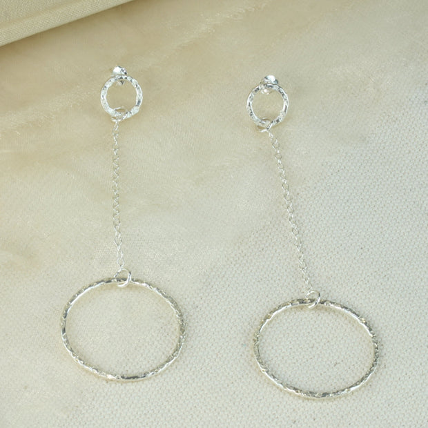 Silver earrings featuring a small hoop at the top with a stud attached to go through the ear. Chain is attached to the small hoop with a jump ring. At the bottom a larger hoop is featured. The hoops have a hammered texture and a sparky shiny finish. A matching y necklace is available.