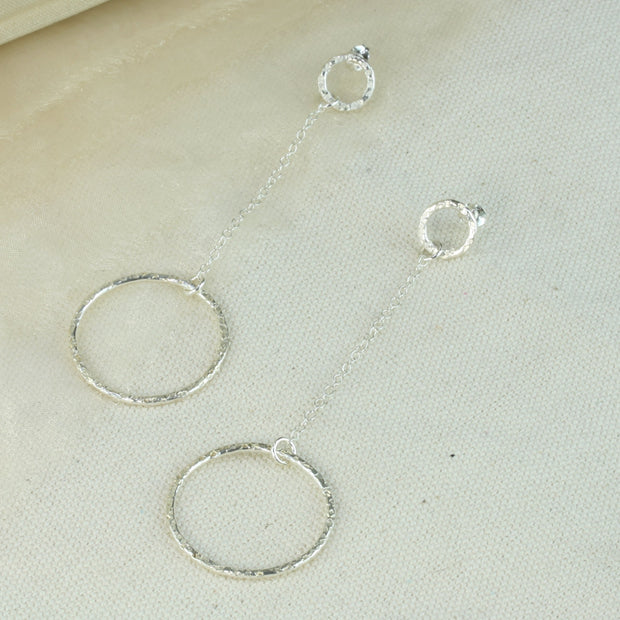 Silver earrings featuring a small hoop at the top with a stud attached to go through the ear. Chain is attached to the small hoop with a jump ring. At the bottom a larger hoop is featured. The hoops have a hammered texture and a sparky shiny finish. A matching y necklace is available.