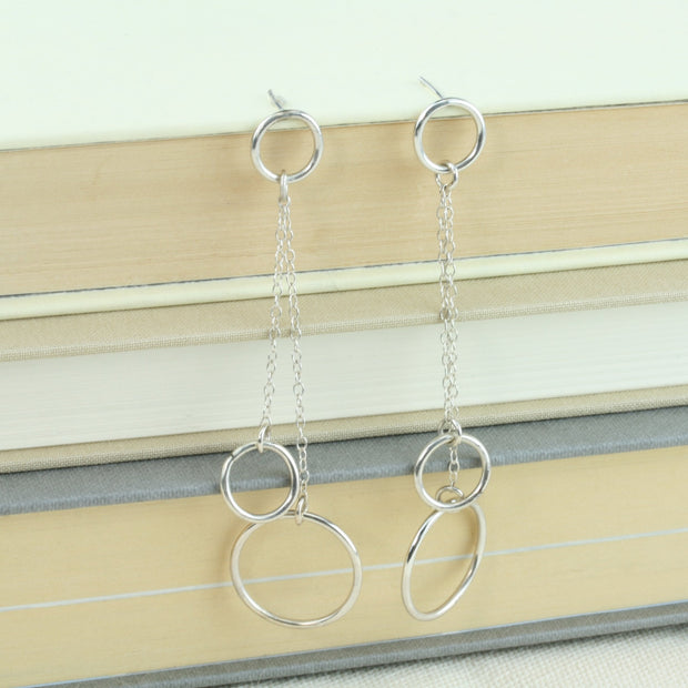 Silver drop earrings featuring two smaller hoops and one larger hoop. One smaller hoop is the stud earring to which the other two hoops are attached. They&