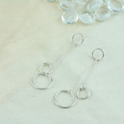 Silver drop earrings featuring two smaller hoops and one larger hoop. One smaller hoop is the stud earring to which the other two hoops are attached. They're attached with a jump ring which holds two chains in place to which the two hoops are attached. The smaller one sits above the larger hoop.