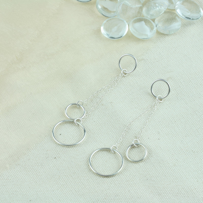 Silver drop earrings featuring two smaller hoops and one larger hoop. One smaller hoop is the stud earring to which the other two hoops are attached. They&