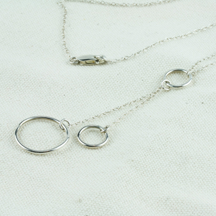 Silver necklace featuring two smaller hoops and one larger hoop. The necklace is looped through a smaller hoop. The other two hoops are attached to the hoop with a jump ring. This holds two short bits of chain in place to which the two hoops are attached.