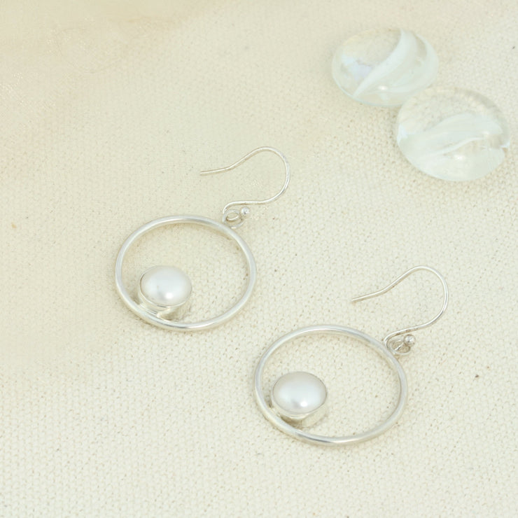 Silver hoop hook earrings featuring a freshwater pearl. The  pearl is 8mm in diameter and is set in a cabochon setting at the bottom on the inside of the hoop. These are handmade earrings, made form eco-silver.