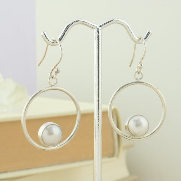 Silver hoop hook earrings featuring a freshwater pearl. The pearl is 8mm in diameter and is set in a cabochon setting at the bottom on the inside of the hoop. These are handmade earrings, made form eco-silver.