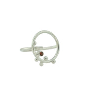Eco silver ring featuring a hoop of 2cm in diameter. With 6 silver balls at the top, and a Garnet gemstone in the middle. The gemstone is 3mm in diameter and the ring has a slight matte finish. The band is open and attached to one side of the hoop, this makes the ring slightly flexible in size.
