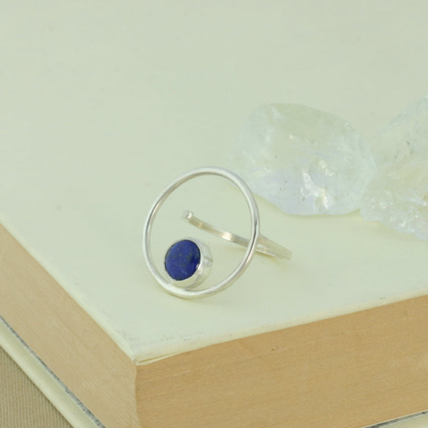 Silver ring featuring a hoop which is 2cm in diameter. The ring band is attached on one side of the ring, leaving the other side open and slightly adjustable. The hoop features a cabochon gemstone which is 8mm in diameter. This ring features a Lapis Lazul gemstone. 