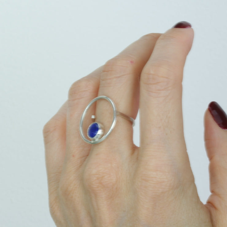 Silver ring featuring a hoop which is 2cm in diameter. The ring band is attached on one side of the ring, leaving the other side open and slightly adjustable. The hoop features a cabochon gemstone which is 8mm in diameter. This ring features a Lapis Lazul gemstone.