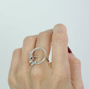 Eco silver ring featuring a hoop of 2cm in diameter. With 6 silver balls at the top, and a Garnet gemstone in the middle. The gemstone is 3mm in diameter and the ring has a slight matte finish. The band is open and attached to one side of the hoop, this makes the ring slightly flexible in size.
