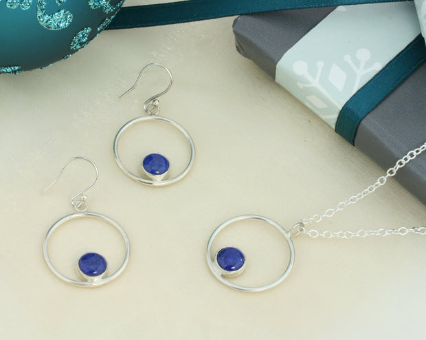 Silver hoop hook earrings featuring a Lapis Lazul gemstone. The gemstone is 8mm in diameter and is set in a cabochon setting at the bottom on the inside of the hoop. These are handmade earrings, made form eco-silver. Shown here with the matching pendant necklace.