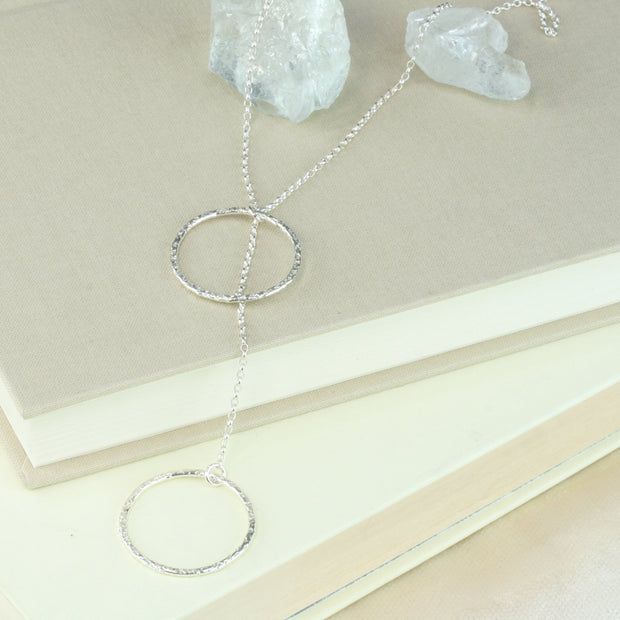 Silver y necklace featuring a hoop at either end of the chain. The hoops have been flattened and given a hammered texture and shiny finish. The chain loops through one of the hoops. By pulling the lower hoop you can adjust how high or low it sits.